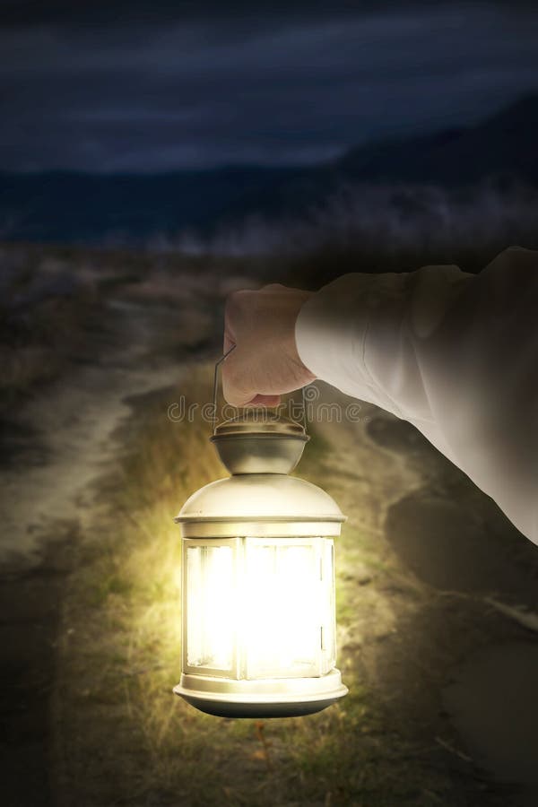 Right hand holding light illuminating dark road at night