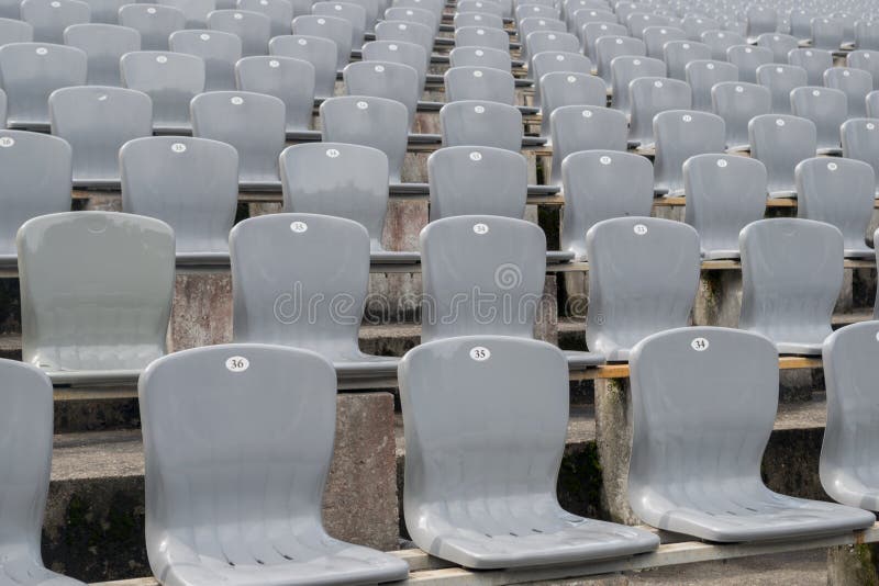 Rijen grijze plastic stoelen met cijfers op de rug die op rijen op cementtafels in het straatgebied zijn geïnstalleerd, met een se