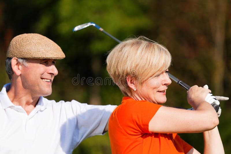 Senior couple playing golf on a summer afternoon, the male partner is trainer to the female golfer. Senior couple playing golf on a summer afternoon, the male partner is trainer to the female golfer