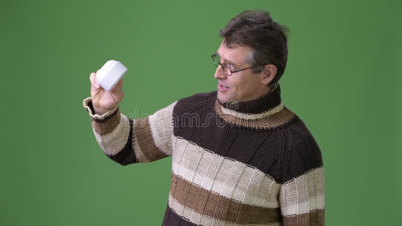 Rijpe knappe mens die colsweater dragen tegen groene achtergrond