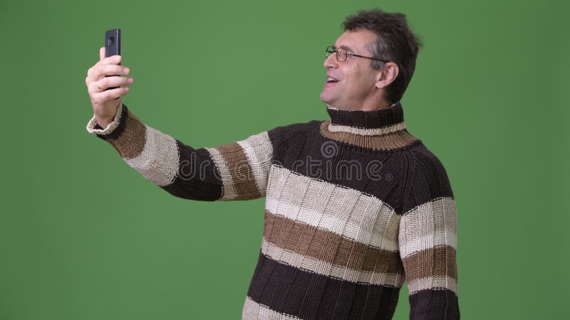 Rijpe knappe mens die colsweater dragen tegen groene achtergrond