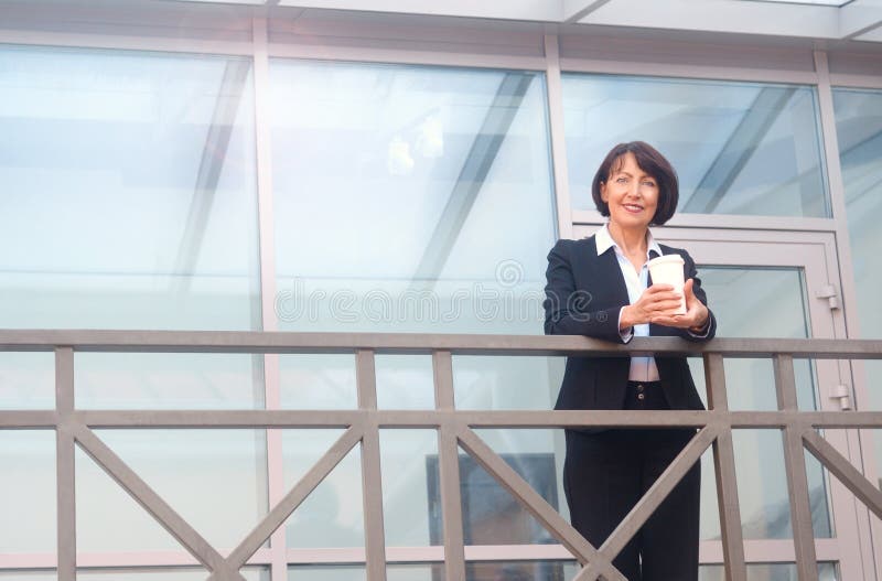 Rijpe onderneemster die een onderbreking voor een bureaugebouw hebben, die op de de telefoon en het drinken koffie spreken stock foto's Rijpe onderneemster die een onderbreking voor een bureaugebouw hebben, die op de de telefoon en het drinken koffie spreken stock foto's