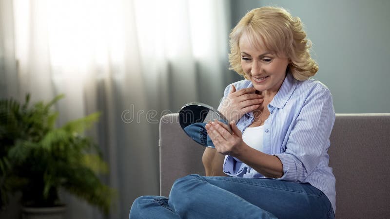 Rijpe vrouw die een handspiegel onderzoeken, die van bezinning, anti-leeftijdsschoonheidsmiddelen genieten stock foto's Rijpe vrouw die een handspiegel onderzoeken, die van bezinning, anti-leeftijdsschoonheidsmiddelen genieten stock foto's