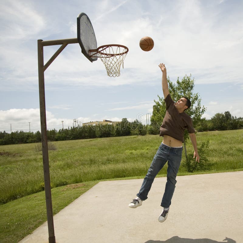 Young man jumping up to rebound a goal on a bright sunny day on an outdoor basketball court. Young man jumping up to rebound a goal on a bright sunny day on an outdoor basketball court.