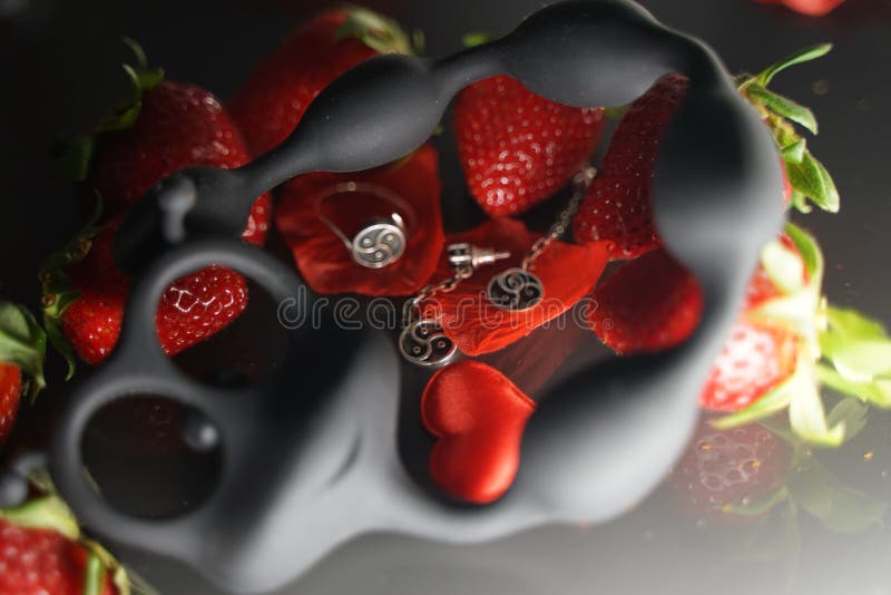 Ring und Ohrringe mit dem Symbol von bdsm liegend unter den Erdbeeren nahe bei dem Sexspielzeuggleiskettenfahrzeug lizenzfreie stockfotografie Ring und Ohrringe mit dem Symbol von bdsm liegend unter den Erdbeeren nahe bei dem Sexspielzeuggleiskettenfahrzeug lizenzfreie stockfotografie