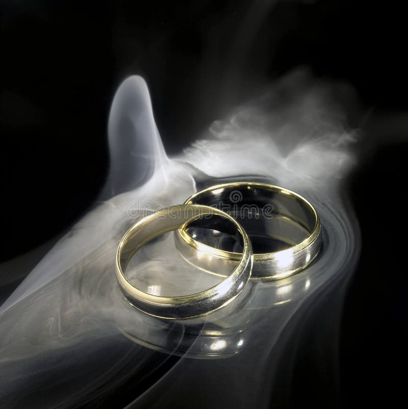 Studio photography of two golden wedding rings and smoke in black reflective back. Studio photography of two golden wedding rings and smoke in black reflective back