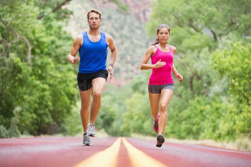 Running young people - two runners jogging on road in nature training for marathon run. Multicultural couple - asian mixed race beautiful model women and caucasian male fitness model exercising. Running young people - two runners jogging on road in nature training for marathon run. Multicultural couple - asian mixed race beautiful model women and caucasian male fitness model exercising