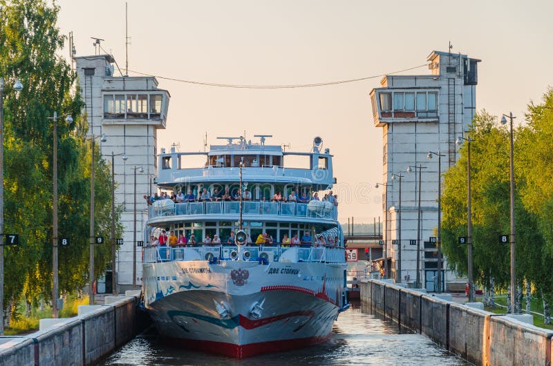 Rio de Sheksna, Rússia - 07 19 2018: As passagens dos capitais do navio de cruzeiros dois do passageiro através da entrada da com imagem de stock Rio de Sheksna, Rússia - 07 19 2018: As passagens dos capitais do navio de cruzeiros dois do passageiro através da entrada da com imagem de stock