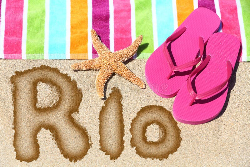 Rio scritto sulla sabbia della spiaggia con un asciugamano variopinto fotografie stock libere da diritti Rio scritto sulla sabbia della spiaggia con un asciugamano variopinto fotografie stock libere da diritti