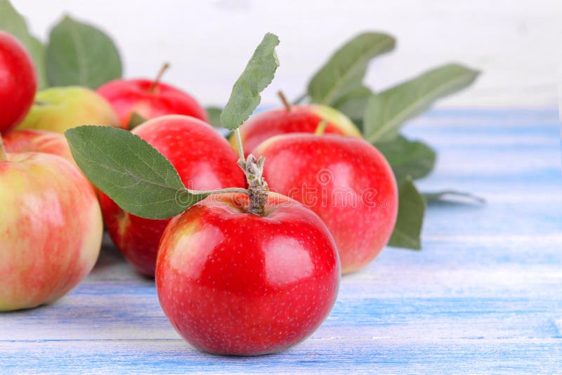 ripe apple with green leaves close-up and lots of apples in the background on a blue wooden background