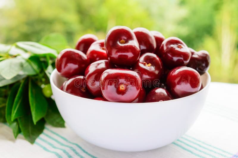 Ripe black cherries in a white bowl on a background of nature. stock photo