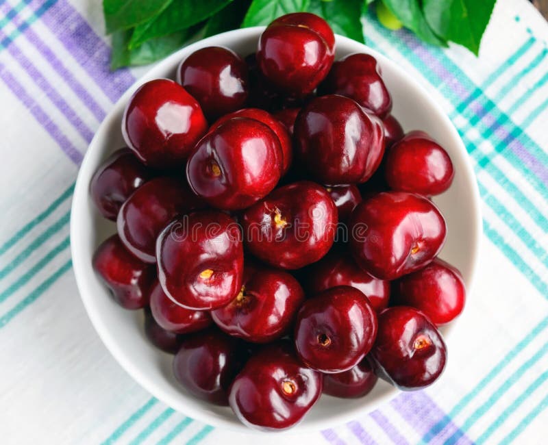 Ripe black cherries in a white bowl on a light background. stock photo