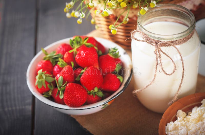 Ripe fresh strawberries, milk in a jug and homemade cottage cheese on the kitchen table.