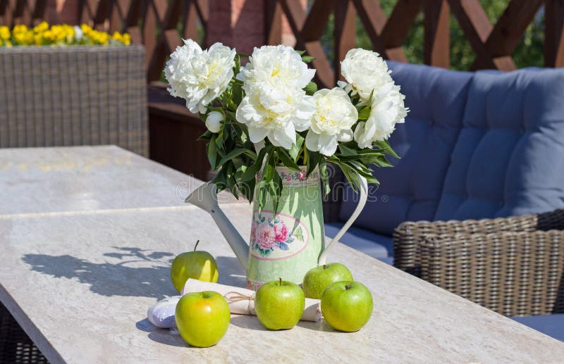 Ripe green apples and a vase of peonies on a marble table
