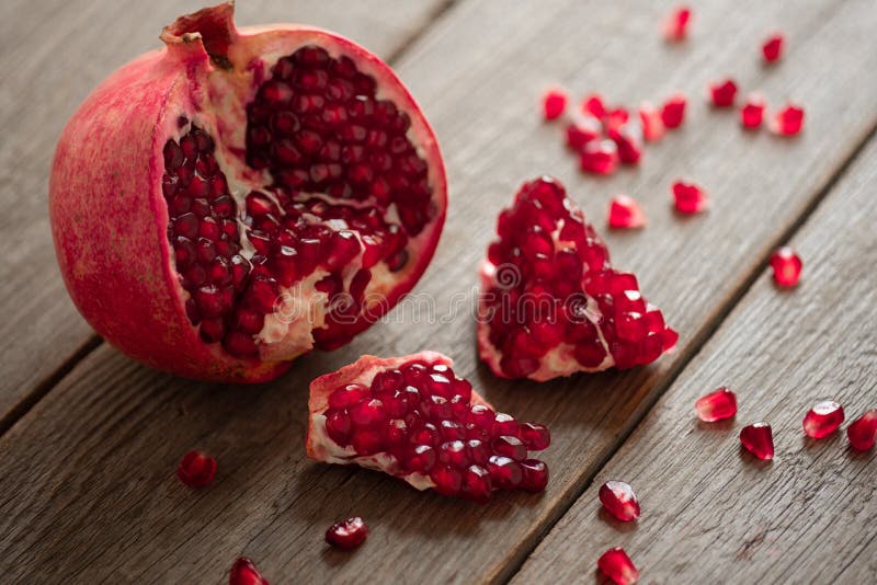 Ripe open pomegranate on a wooden table red grains are scattered around