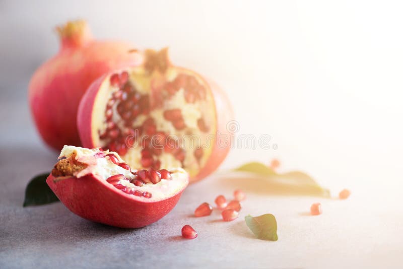 Ripe pomegranate fruit with green leaves on grey concrete background. Banner with copy space. Sunny bokeh effect royalty free stock photo Ripe pomegranate fruit with green leaves on grey concrete background. Banner with copy space. Sunny bokeh effect royalty free stock photo
