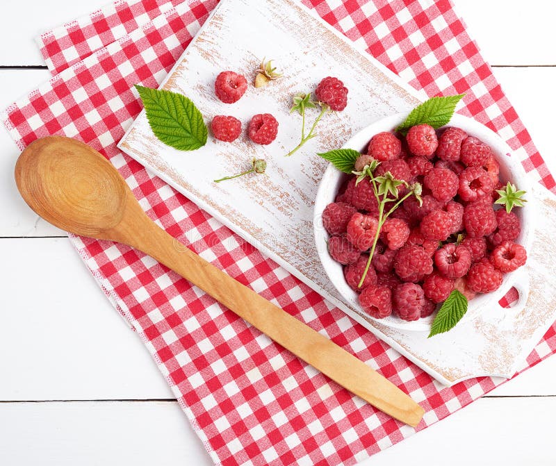 ripe red raspberries in a white wooden plate on a table