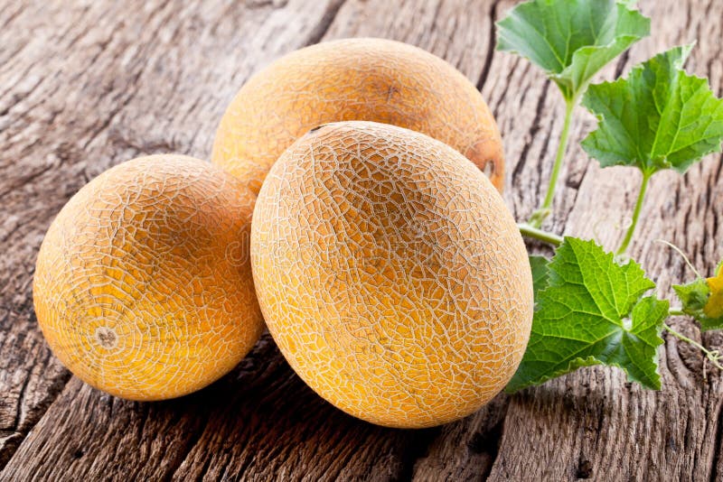 Ripes melons with melon leaves on wooden background.