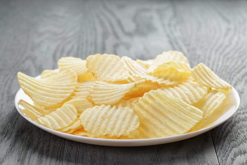 Rippled potato chips in white plate on wood table