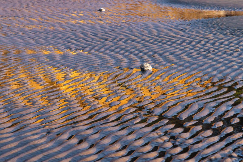 Rippled structures on a sandy beach with golden reflections of a cliff at sunset royalty free stock photography