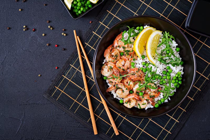 Ris med unga gröna ärtor, räkor och arugula i svart bunke royaltyfri bild Ris med unga gröna ärtor, räkor och arugula i svart bunke royaltyfri bild