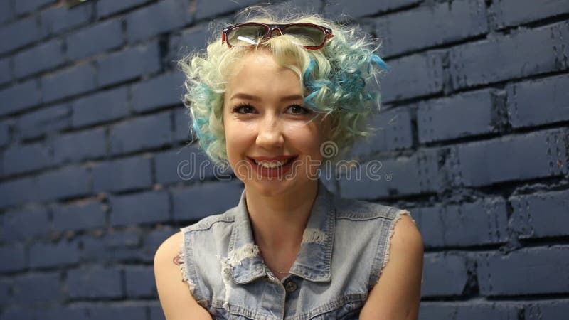 Risa sonriente de la muchacha cabelluda rizada feliz alegre joven mirando la cámara sobre fondo de la pared de ladrillo almacen de video