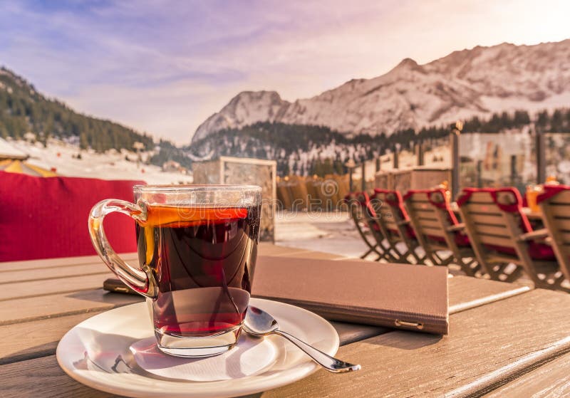 Image with a hot drink and a restaurant menu, on a wooden table, on a sunny winter day, mountains in the background. Picture taken in Austria. Image with a hot drink and a restaurant menu, on a wooden table, on a sunny winter day, mountains in the background. Picture taken in Austria.