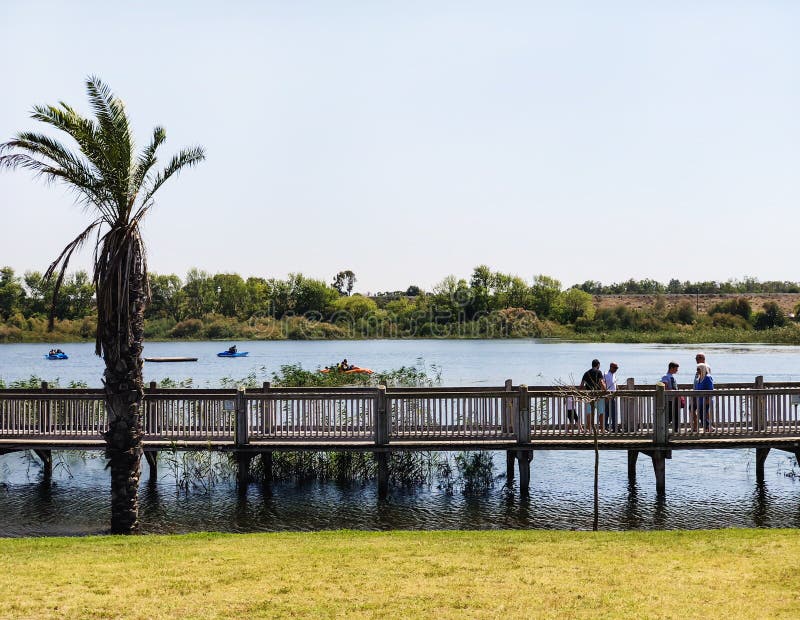 RISHON LE ZION, ISRAEL -APRIL 14, 2018: People walk along a wooden walking bridge near the lake in Rishon Lezion, Israel.