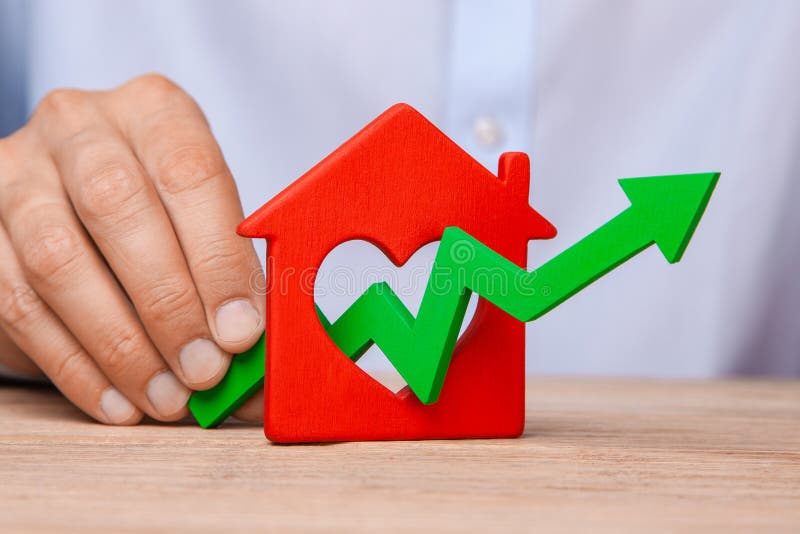 Rising house prices. Man is holding green arrow up in hand and house on the table royalty free stock photography Rising house prices. Man is holding green arrow up in hand and house on the table royalty free stock photography