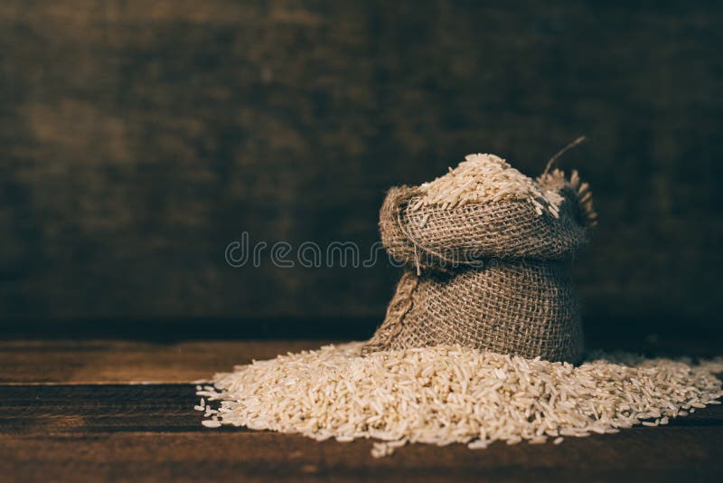 Riso sbramato non lucidato naturale in un piccolo sacco della tela da imballaggio sulla tavola di legno sopra fondo scuro fotografia stock libera da diritti Riso sbramato non lucidato naturale in un piccolo sacco della tela da imballaggio sulla tavola di legno sopra fondo scuro fotografia stock libera da diritti