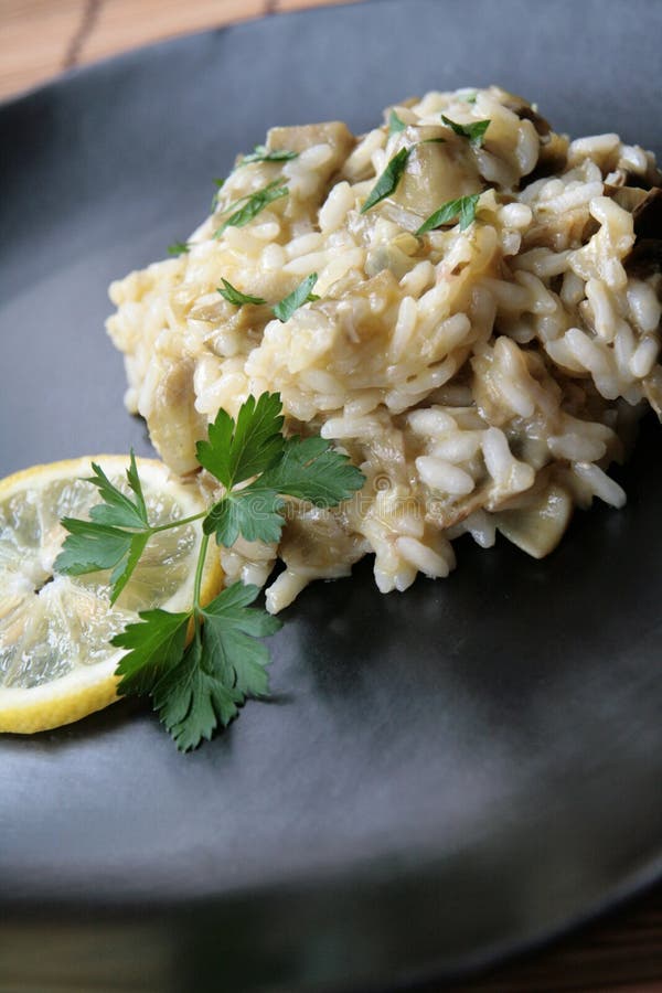 Close-up of a dish of risotto with artichokes in a black plate, decorated with parsley and a slice of lemon