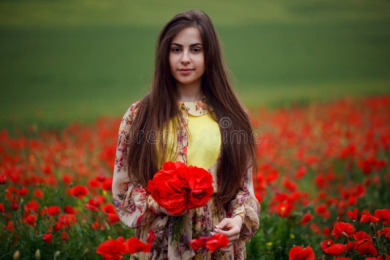 Close up portrait of hair long young woman with flower poppy, holdings in hands a bouquet of a red flowers