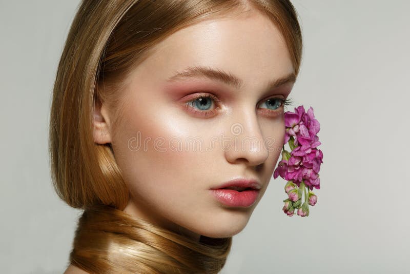 Ritratto alto vicino della ragazza con gli occhi azzurri, trucco luminoso, collo avvolto in capelli, fiori porpora arricciati in fotografie stock Ritratto alto vicino della ragazza con gli occhi azzurri, trucco luminoso, collo avvolto in capelli, fiori porpora arricciati in fotografie stock