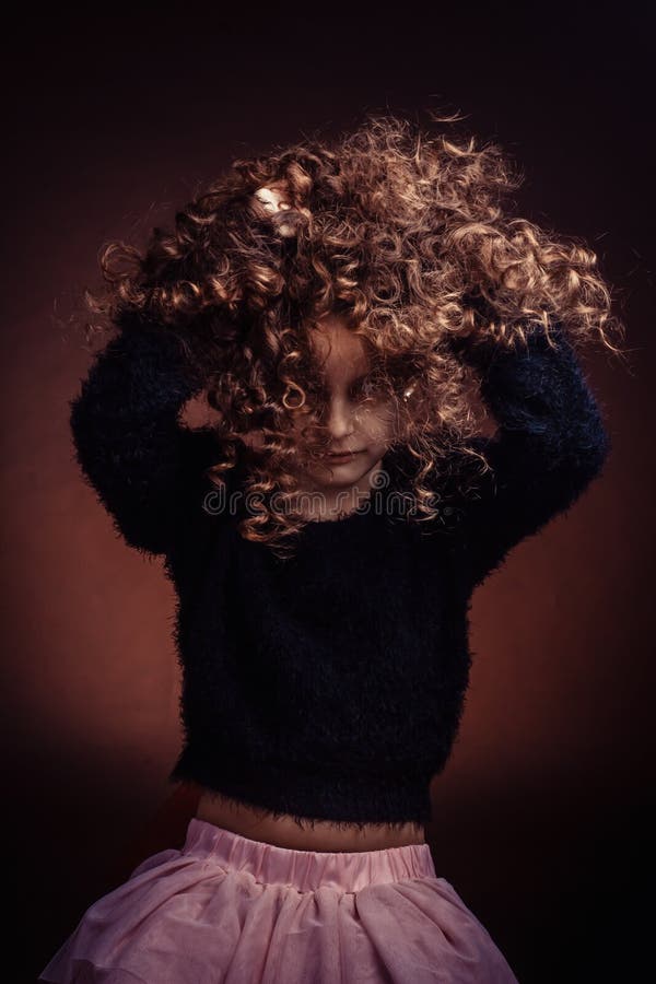 Ritratto da studio di una bambina, una bambina che gioca con i suoi lunghi capelli ricci immagine stock Ritratto da studio di una bambina, una bambina che gioca con i suoi lunghi capelli ricci immagine stock