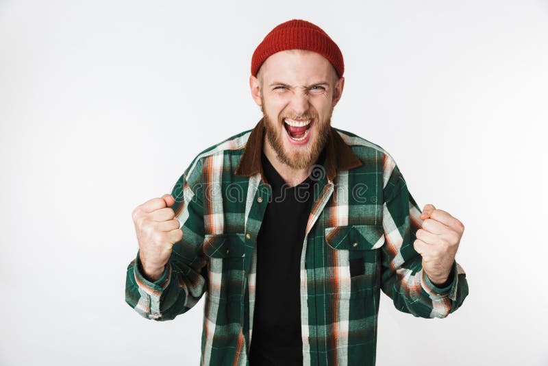 Ritratto del cappello emozionante dell'uomo 20s e della camicia di plaid d'uso che gridano, mentre stando isolato sopra fondo bia immagine stock Ritratto del cappello emozionante dell'uomo 20s e della camicia di plaid d'uso che gridano, mentre stando isolato sopra fondo bia immagine stock