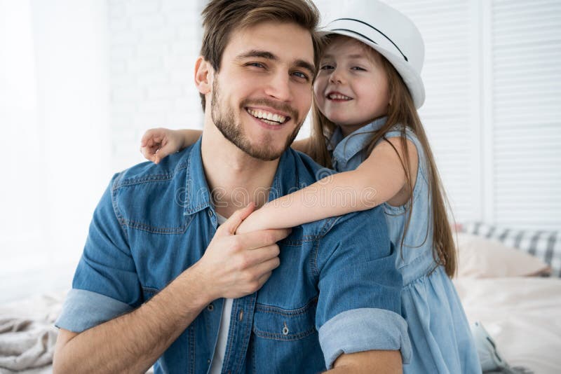 Ritratto del padre bello e sua della figlia sveglia che abbracciano, esaminanti macchina fotografica e sorridenti mentre sedendos immagini stock Ritratto del padre bello e sua della figlia sveglia che abbracciano, esaminanti macchina fotografica e sorridenti mentre sedendos immagini stock
