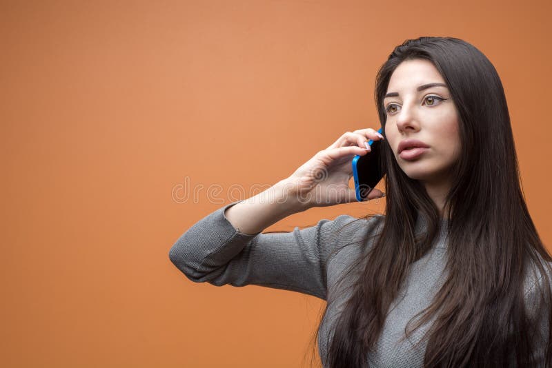 Ritratto del primo piano di giovane bella donna pensierosa castana che tiene il suo smartphone e che ascolta, pensante a qualcosa fotografia stock Ritratto del primo piano di giovane bella donna pensierosa castana che tiene il suo smartphone e che ascolta, pensante a qualcosa fotografia stock
