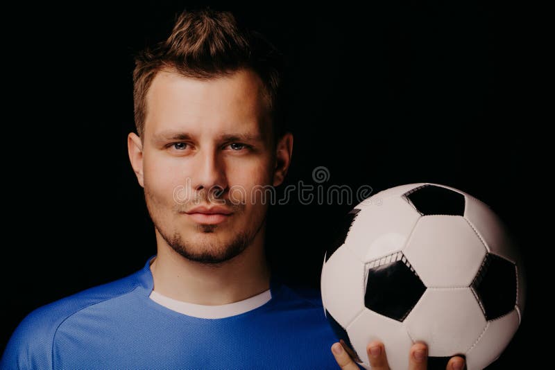 Ritratto del primo piano di giovane calcio bello del giocatore di football americano che posa sul fondo scuro immagini stock libere da diritti Ritratto del primo piano di giovane calcio bello del giocatore di football americano che posa sul fondo scuro immagini stock libere da diritti