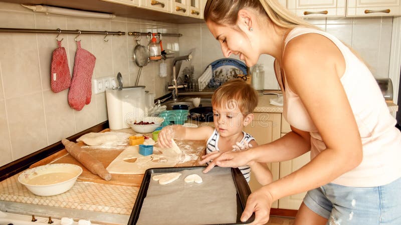 Ritratto del primo piano di giovane madre con la teglia da forno della tenuta del ragazzo del bambino ed i biscotti di fabbricazi fotografia stock libera da diritti Ritratto del primo piano di giovane madre con la teglia da forno della tenuta del ragazzo del bambino ed i biscotti di fabbricazi fotografia stock libera da diritti