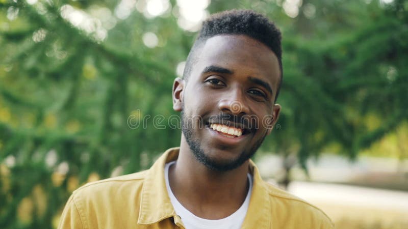 Ritratto del primo piano del movimento lento dell'uomo afroamericano allegro che sorride e che esamina macchina fotografica all'a