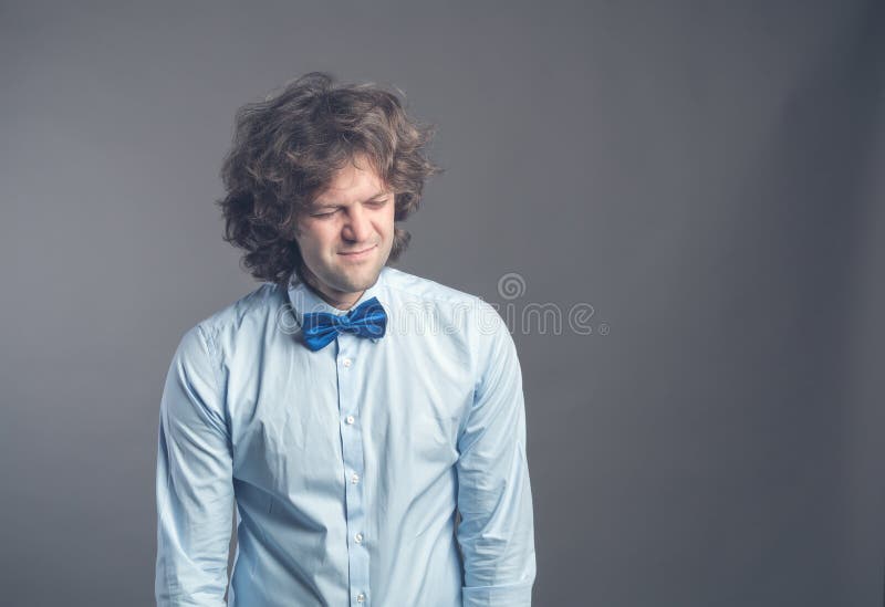 Ritratto del tipo triste esaurito con capelli irsuti che stanno e che guardano giù con la apatia Isolato sul blu d'uso del fondo immagini stock Ritratto del tipo triste esaurito con capelli irsuti che stanno e che guardano giù con la apatia Isolato sul blu d'uso del fondo immagini stock