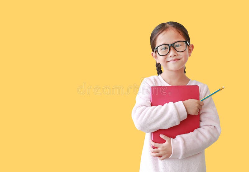 Ritratto dell'abbraccio d'uso sorridente del monocolo della scolara asiatica un libro e giudicare una matita a disposizione isola immagine stock Ritratto dell'abbraccio d'uso sorridente del monocolo della scolara asiatica un libro e giudicare una matita a disposizione isola immagine stock