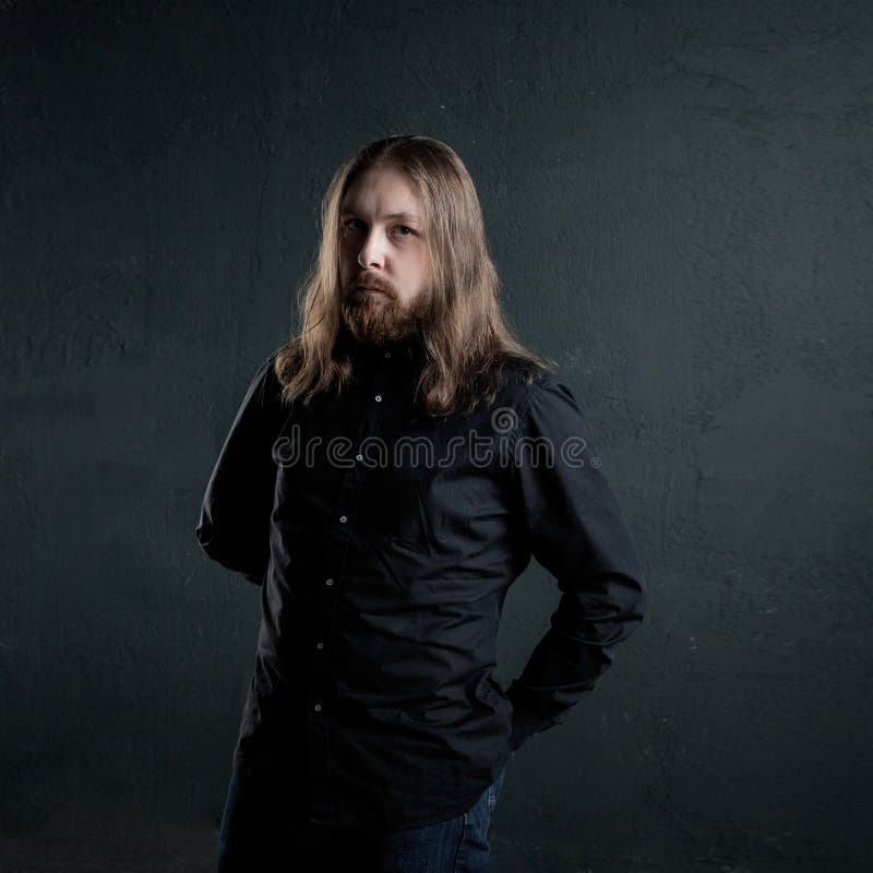 Ritratto dell'uomo con capelli lunghi e della barba in vestiti neri su fondo scuro fotografia stock Ritratto dell'uomo con capelli lunghi e della barba in vestiti neri su fondo scuro fotografia stock