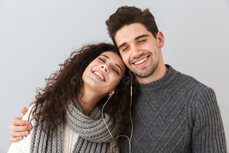 Ritratto dell'uomo e della donna sorridenti delle coppie che ascoltano la musica insieme alle cuffie, isolato sopra fondo grigio fotografia stock