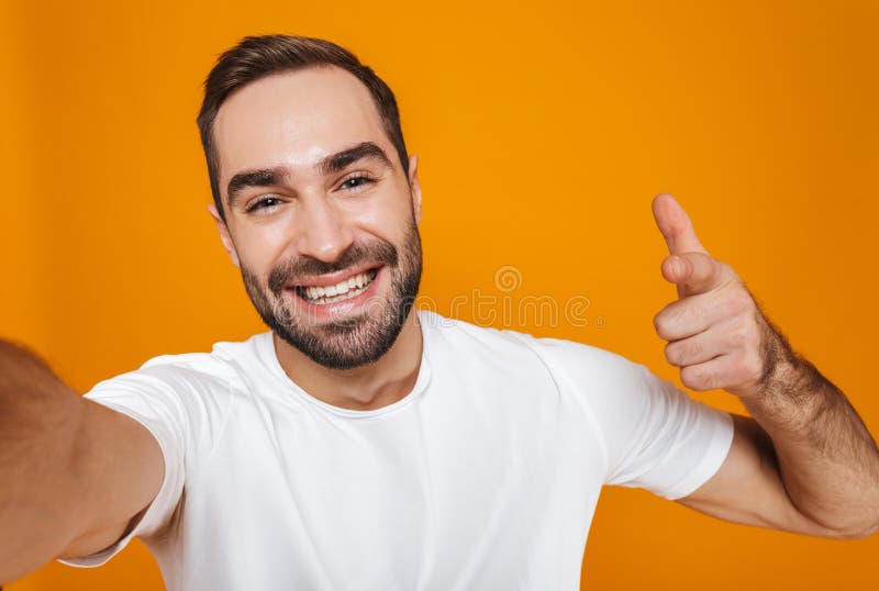 Ritratto dell'uomo ottimista 30s in maglietta che ride mentre prendendo la foto del selfie, isolato sopra fondo giallo immagine stock Ritratto dell'uomo ottimista 30s in maglietta che ride mentre prendendo la foto del selfie, isolato sopra fondo giallo immagine stock