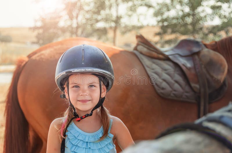 Ritratto della bambina e del cavallo marrone Ragazza con i caschi immagine stock libera da diritti Ritratto della bambina e del cavallo marrone Ragazza con i caschi immagine stock libera da diritti