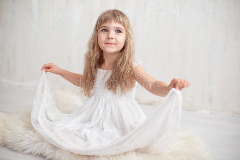 Ritratto della bambina graziosa in vestito bianco, esaminante macchina fotografica e sorridere, stanti contro il fondo grigio immagini stock libere da diritti Ritratto della bambina graziosa in vestito bianco, esaminante macchina fotografica e sorridere, stanti contro il fondo grigio immagini stock libere da diritti