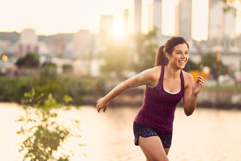 Ritratto della donna millenial attiva che pareggia al crepuscolo con un paesaggio urbano e un tramonto urbani nei precedenti fotografia stock libera da diritti Ritratto della donna millenial attiva che pareggia al crepuscolo con un paesaggio urbano e un tramonto urbani nei precedenti fotografia stock libera da diritti