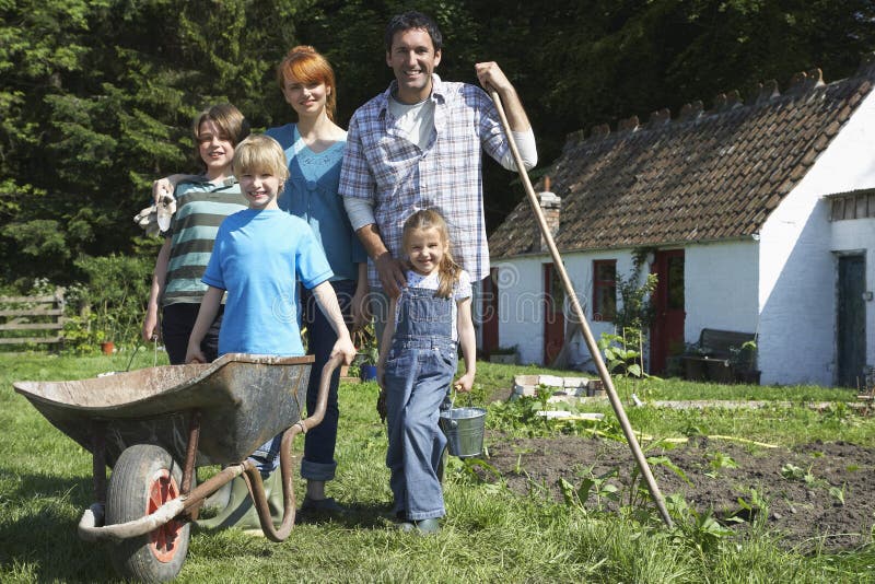 Ritratto della famiglia che fa il giardinaggio fuori del cottage fotografie stock libere da diritti Ritratto della famiglia che fa il giardinaggio fuori del cottage fotografie stock libere da diritti