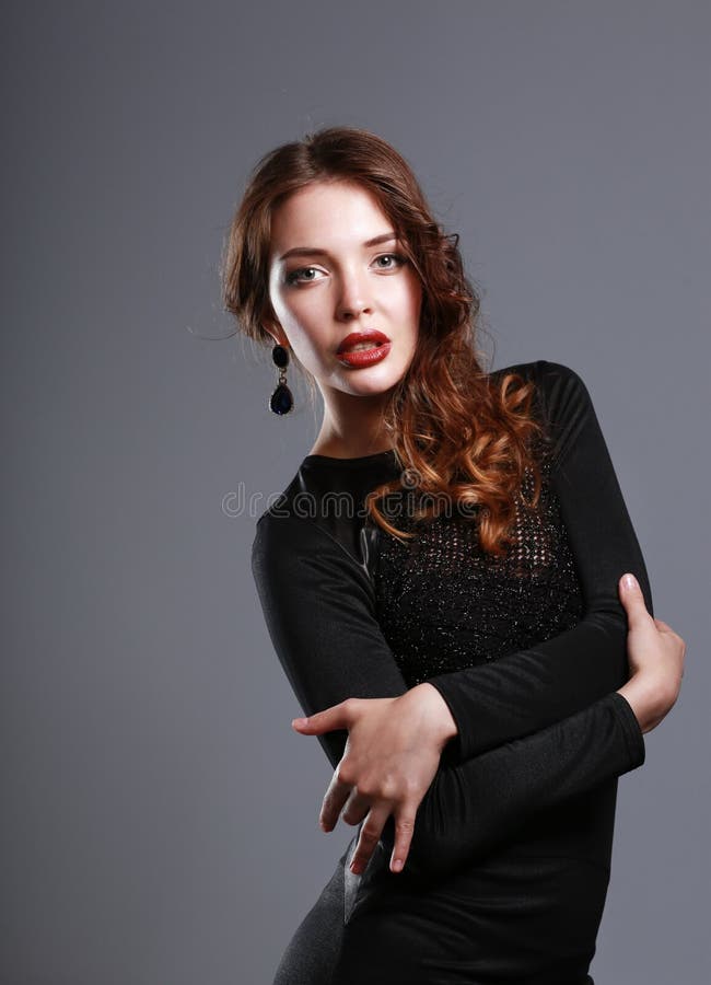 Ritratto della giovane donna felice in vestito nero su fondo grigio fotografia stock Ritratto della giovane donna felice in vestito nero su fondo grigio fotografia stock